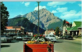 Main Street Canadian Rockies Banff Canada with Floral Planters Old Cars Postcard - $9.85