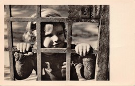 YOUNG GIRL LOOKING THROUGH HEAVY METAL GATE-GERMAN PHOTO POSTCARD - £4.26 GBP